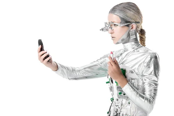 Visão lateral do robô de prata segurando batom e olhando para o espelho isolado em branco, conceito de tecnologia futuro — Fotografia de Stock