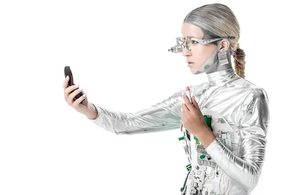 Side view of silver robot holding lipstick and looking at mirror isolated on white, future technology concept — Stock Photo