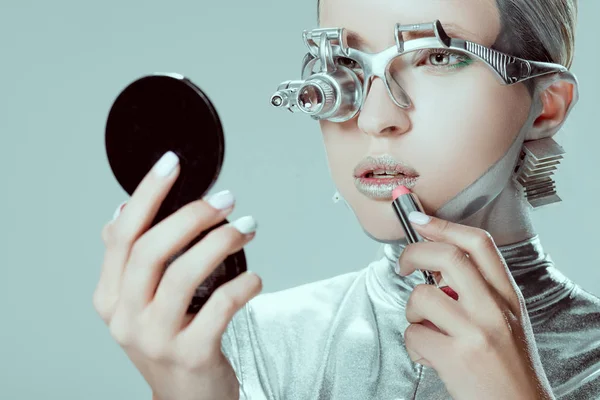 Robot d'argento che si guarda allo specchio e applica rossetto isolato sul grigio, concetto tecnologico futuro — Foto stock