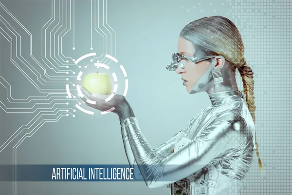 Side view of cyborg holding and examining green apple with digital data isolated on grey with 