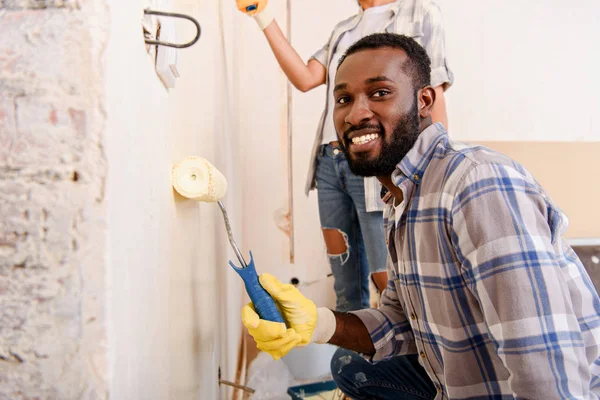 Красивый молодой человек рисует стену с женой во время ремонта дома — стоковое фото