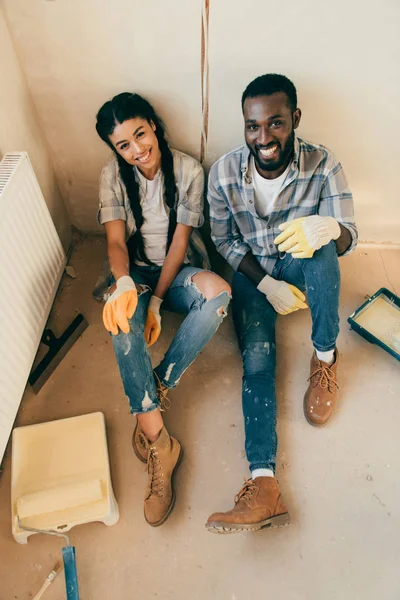 Vue grand angle du couple assis sur le sol et regardant la caméra pendant la rénovation de la maison — Photo de stock