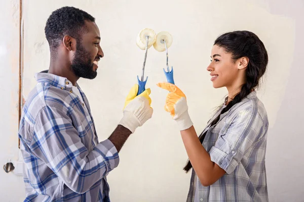 Side view of couple with rolling brushes looking at each other while making renovation of home — Stock Photo