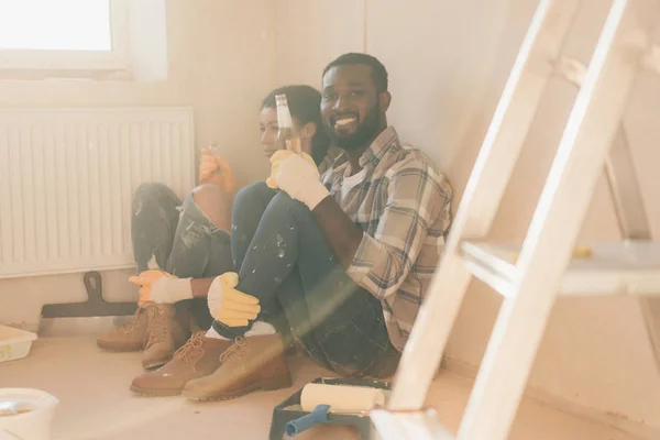 Heureux jeune couple se détendre sur le sol avec de la bière tout en faisant la rénovation de la maison — Photo de stock