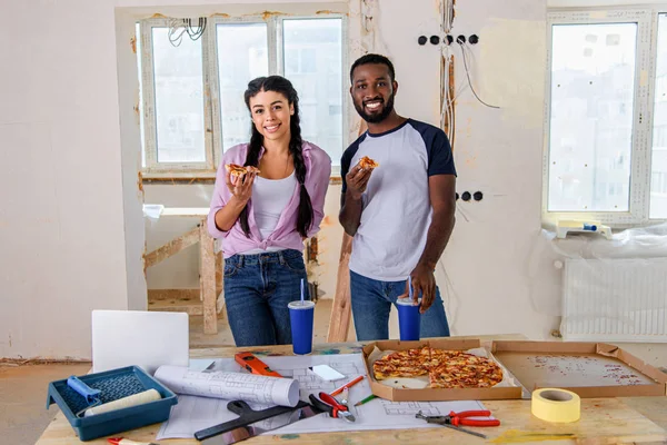 Sorrindo jovem casal comer pizza enquanto faz renovação de casa — Fotografia de Stock