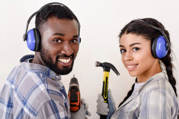 Couple with drill and hammer looking at camera while making renovation of home — Stock Photo