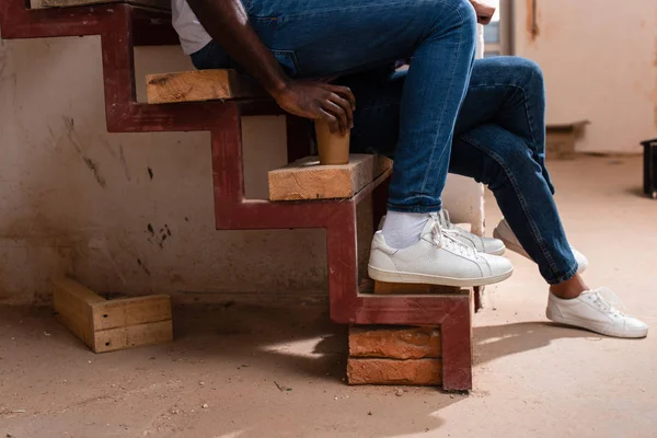 Plan recadré de couple assis sur les escaliers avec tasse de café en papier pendant la rénovation de la maison — Photo de stock