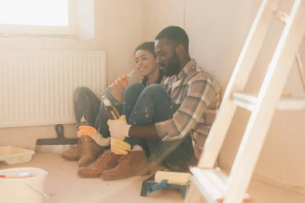 Jeune couple afro-américain boire de la bière sur le sol tout en faisant la rénovation de la maison — Photo de stock