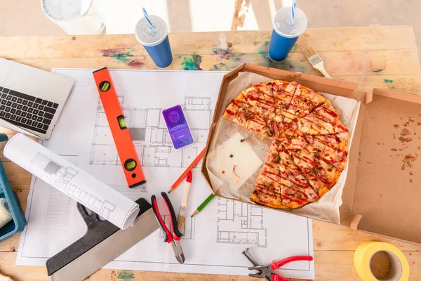 Primer plano de la caja con pizza, herramientas y teléfono inteligente con aplicación de compras en la pantalla en el plan de construcción - foto de stock