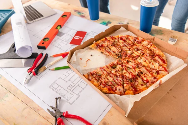 Close-up shot of box with pizza, tools and smartphone with youtube app on screen on building plan — Stock Photo