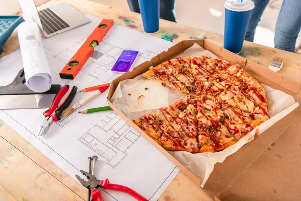 Primer plano de la caja con pizza, herramientas y teléfono inteligente con aplicación de compras en la pantalla en el plan de construcción - foto de stock