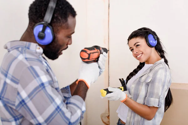Brincalhão jovem casal se divertindo com martelo e broca ao fazer renovação de casa — Fotografia de Stock