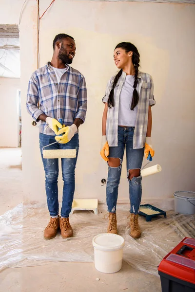Young couple with rolling brushes looking at each other while making renovation of home — Stock Photo