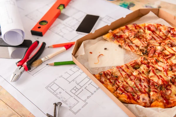 Close-up shot of box with pizza, tools and smartphone on building plan — Stock Photo