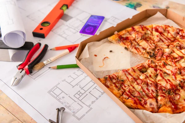 Primer plano de la caja con pizza, herramientas y teléfono inteligente con aplicación de compras en la pantalla en el plan de construcción - foto de stock