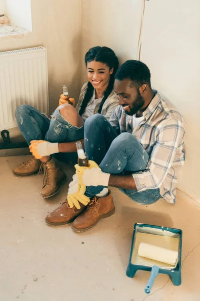 Vista de alto ângulo de casal sentado no chão com cerveja ao fazer renovação de casa — Fotografia de Stock