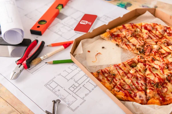 Close-up shot of box with pizza, tools and smartphone with youtube app on screen on building plan — Stock Photo