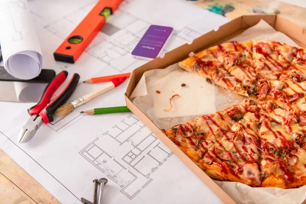 Nahaufnahme einer Box mit Pizza, Werkzeug und Smartphone mit Instagram-App auf dem Bildschirm auf dem Bauplan — Stockfoto