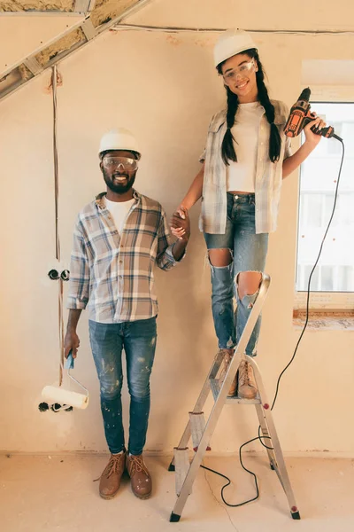 Heureux jeune couple avec échelle faisant la rénovation de la maison ensemble et regardant la caméra — Photo de stock