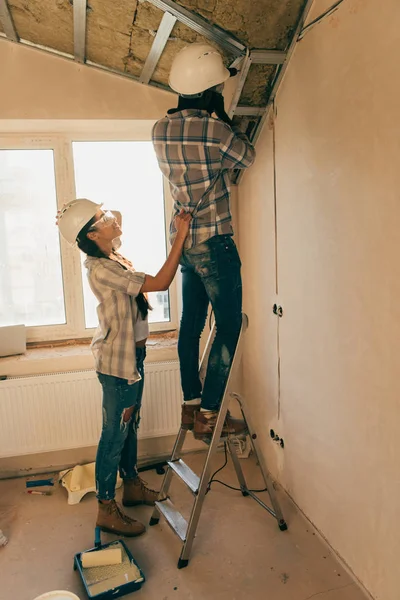 Молода пара в шоломах робить ремонт будинку — стокове фото