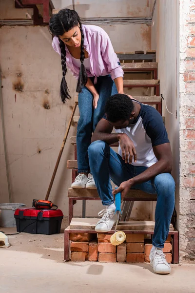 Jeune femme soutenir son mari tandis que son assis sur les escaliers épuisé lors de la rénovation de la maison — Photo de stock