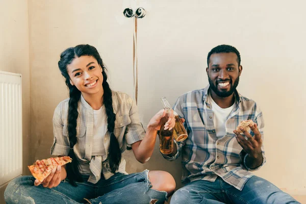 Улыбающаяся пара с пивом и пиццей сидя на полу, делая ремонт дома — стоковое фото