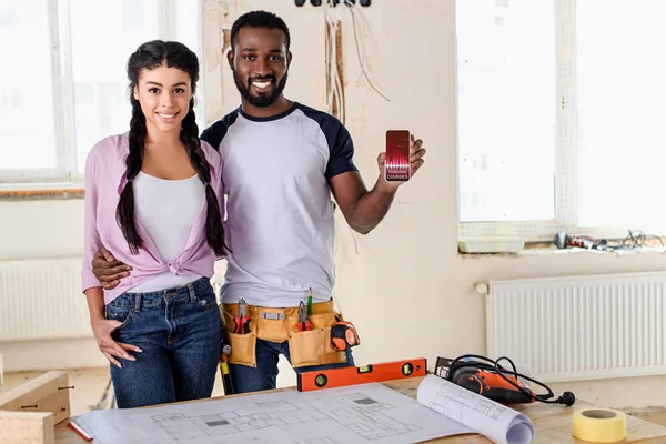 Heureux couple tenant smartphone avec graphique à l'écran pendant la rénovation — Photo de stock