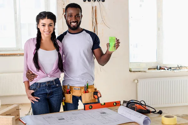 Couple holding smartphone with shopping app on screen during renovation — Stock Photo