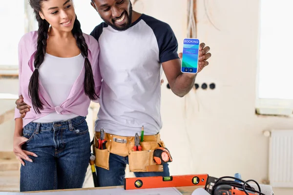 Couple holding smartphone with booking app on screen during renovation — Stock Photo