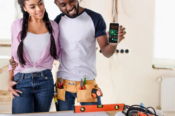 Casal segurando smartphone com gráficos na tela durante a renovação — Fotografia de Stock