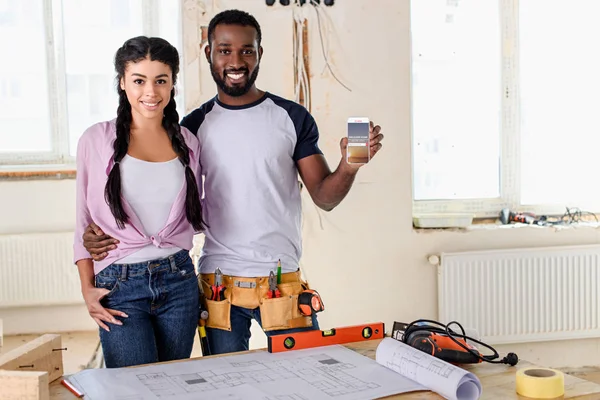 Couple holding smartphone with airbnb on screen during renovation — Stock Photo