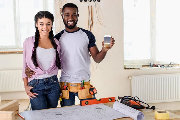 Pareja sosteniendo teléfono inteligente con airbnb en la pantalla durante la renovación — Stock Photo