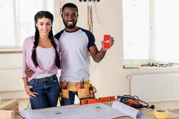 Pareja sosteniendo teléfono inteligente con aplicación de youtube en la pantalla durante la renovación - foto de stock