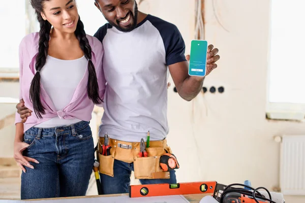 Happy couple holding smartphone with twitter on screen during renovation at new home — Stock Photo