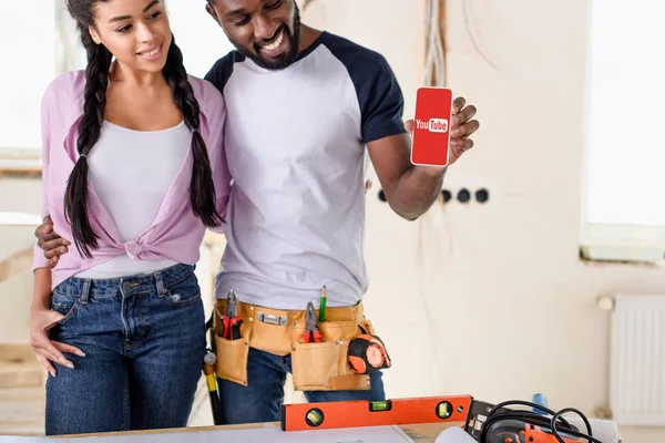 African american couple holding smartphone with youtube on screen during renovation at new home — Stock Photo