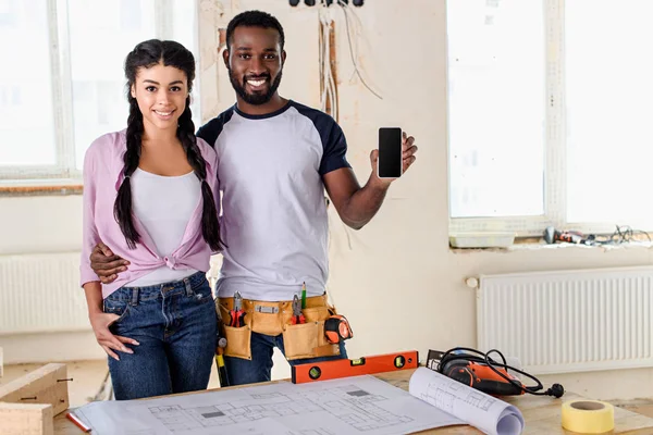 Afrikanisch-amerikanisches Paar zeigt Smartphone mit leerem Bildschirm bei Renovierungsarbeiten im neuen Zuhause — Stockfoto