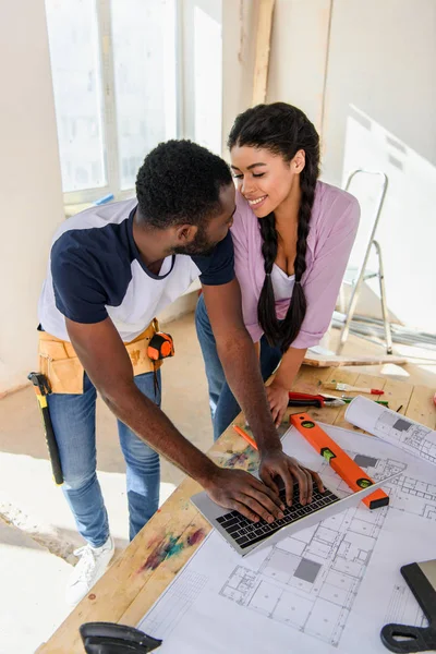 Vista de ángulo alto de la pareja joven usando el ordenador portátil y mirándose entre sí durante la renovación del hogar - foto de stock