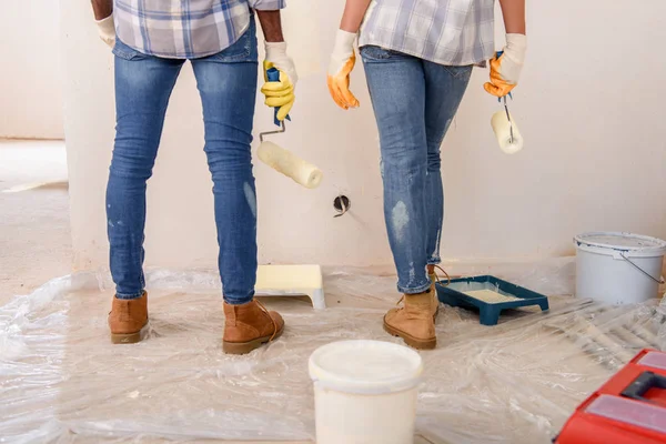 Imagem cortada de casal com rolos de pintura em pé perto da parede pintada na nova casa — Fotografia de Stock