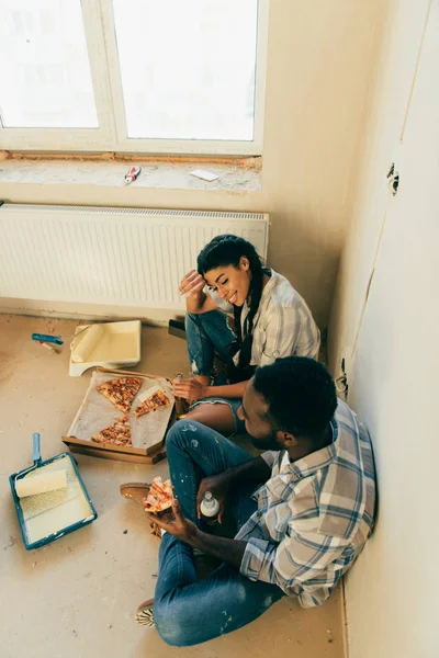High angle view of african american couple eating pizza and drinking beer during renovation at home — Stock Photo