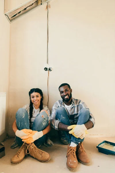 Feliz pareja en guantes de protección mirando a la cámara durante la renovación del hogar - foto de stock