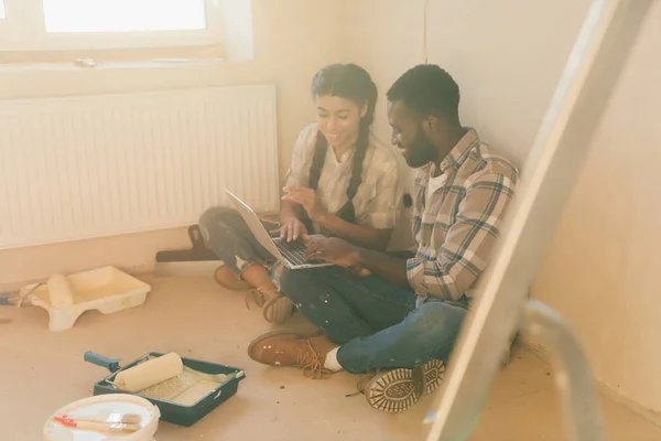Молода усміхнена пара використовує ноутбук під час ремонту нового будинку — стокове фото