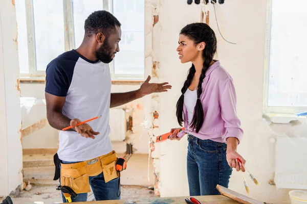 Seitenansicht einer irritierten Frau, die bei Renovierungsarbeiten zu Hause mit ihrem Freund Achselzucken macht — Stockfoto