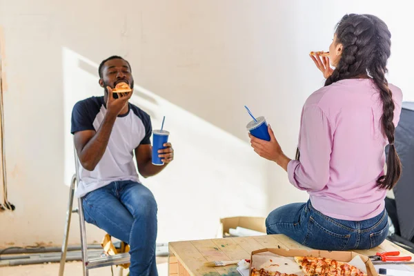 Молодая африканская американская пара обедает с пиццей и содовой во время ремонта — стоковое фото