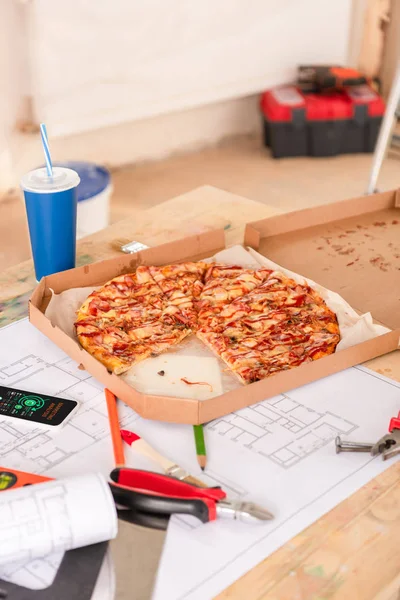 Enfoque selectivo de pizza, refrescos, planos, herramientas y teléfonos inteligentes con gráficos en pantalla en la mesa - foto de stock