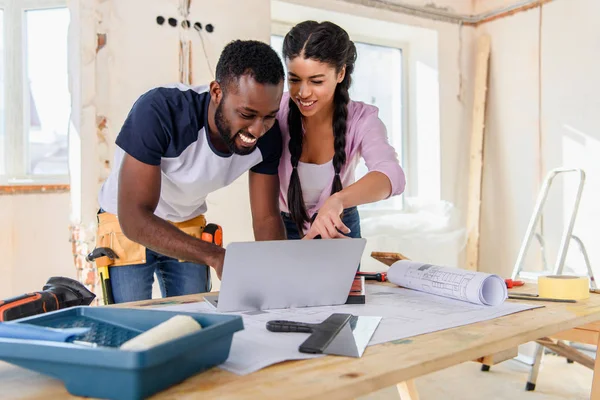 Young african american woman pointing at laptop screen to boyfriend during renovation of home — Stock Photo