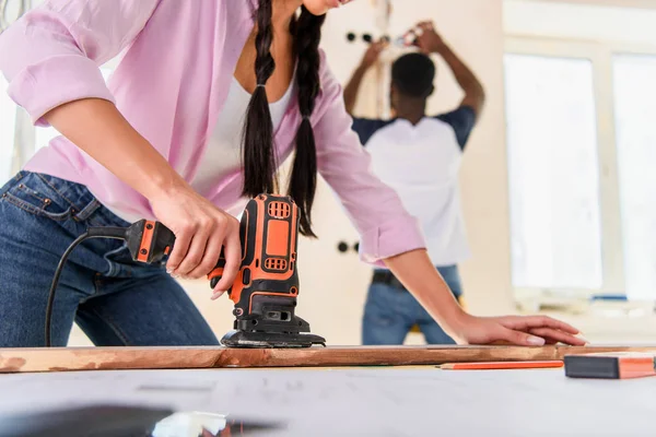 Partial view of woman working with jigsaw while her boyfriend standing behind during renovation at home — Stock Photo