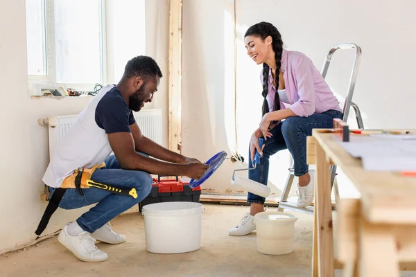 Happy young man sitting near bucket with paint while his girlfriend sitting with paint roller during renovation at home — Stock Photo