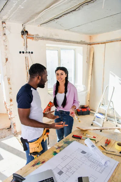 High angle view of young african american couple standing near table with blueprint during renovation of home — Stock Photo