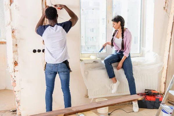 Rear view of man working with pliers while his girlfriend putting paint roller into roller tray on windowsill at new home — Stock Photo