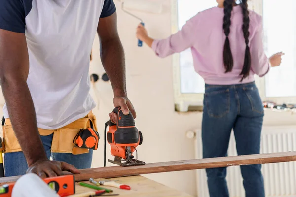 Cropped image of man working with jigsaw while his girlfriend standing behind during renovation at home — Stock Photo